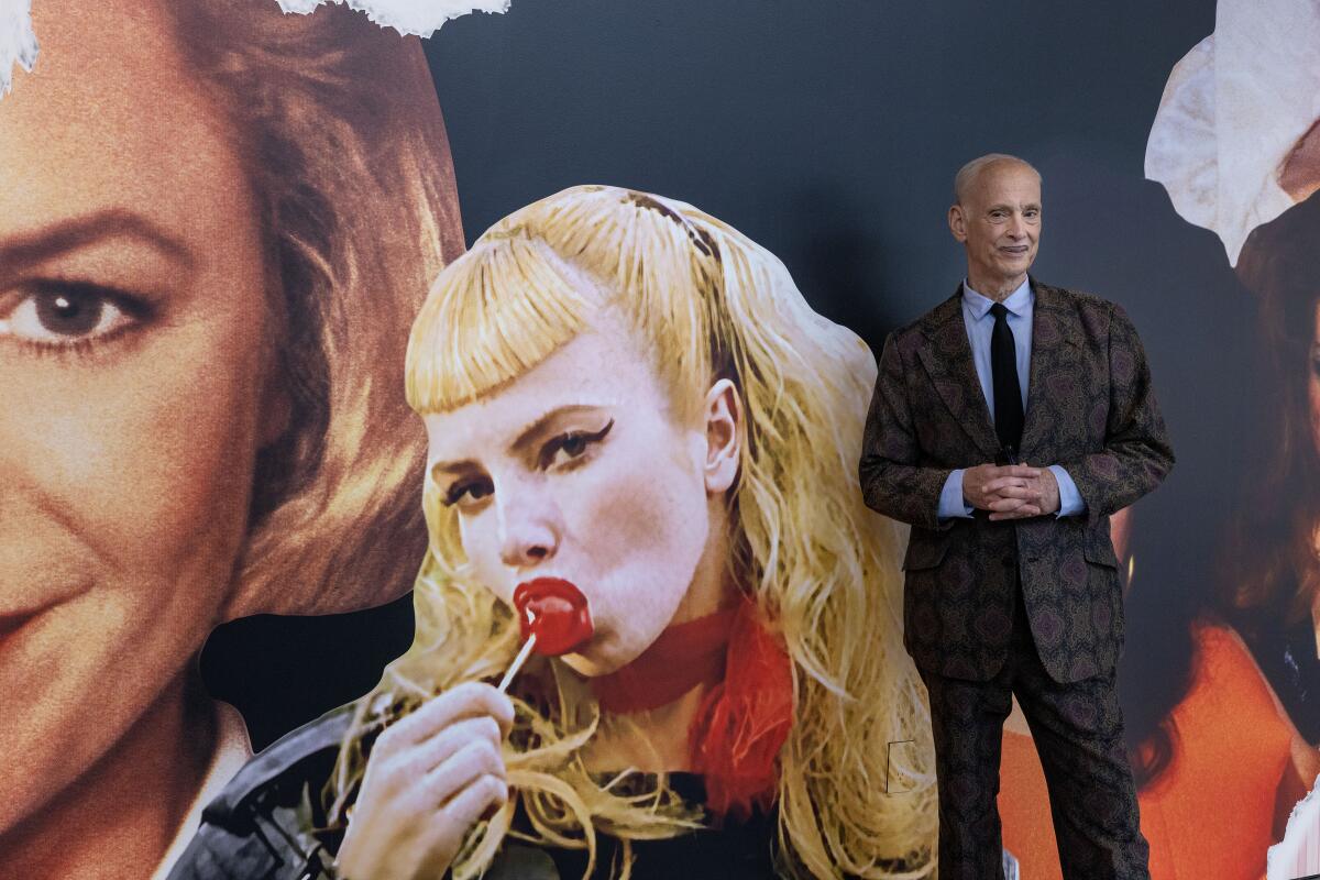 A dapper man in a suit and tie poses in front of a lurid collage.