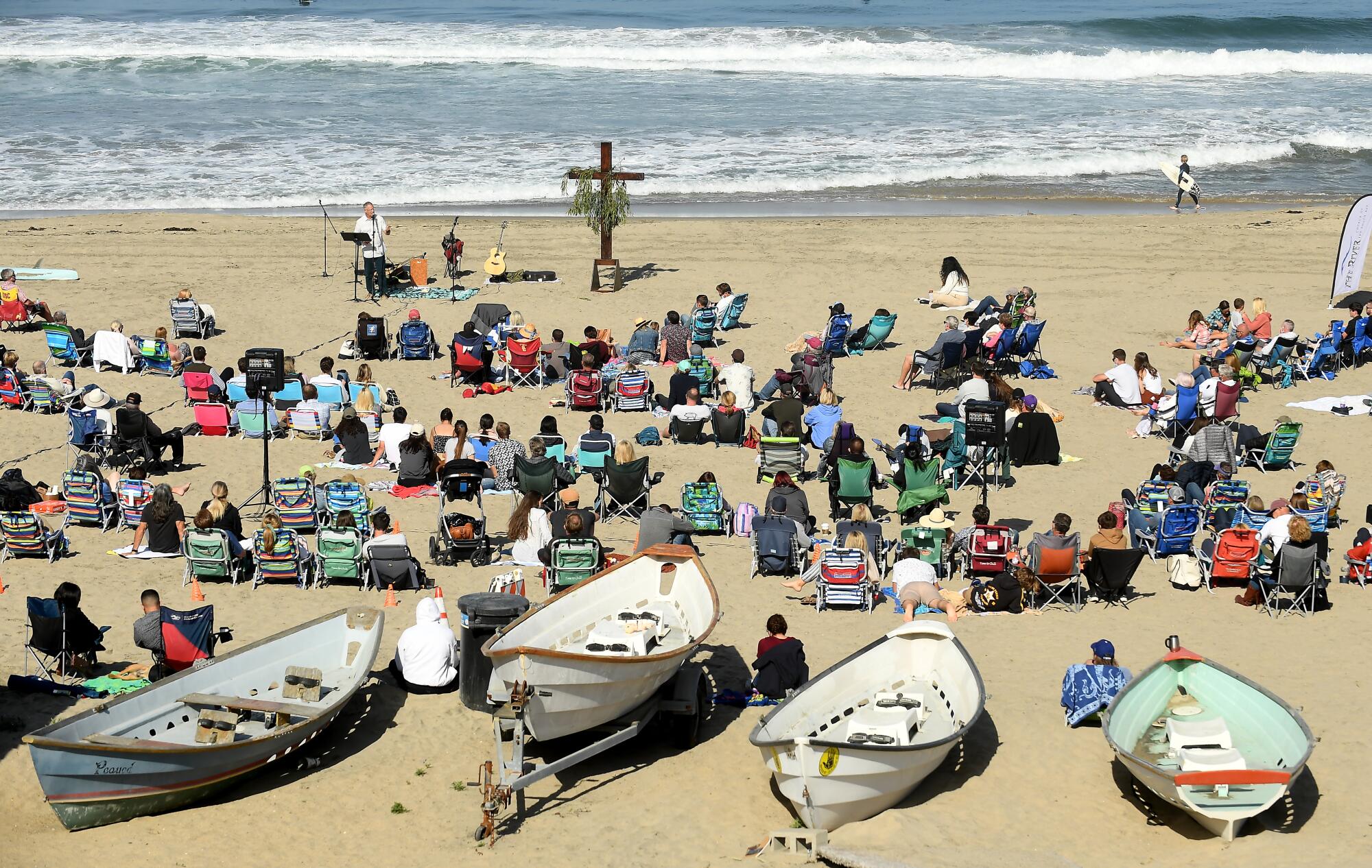 People gather at a beach in front of a cross.