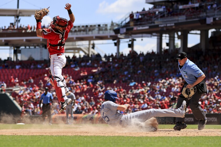 The Dodgers' Cody Bellinger scores a run on a hit by Freddie Freeman as Cincinnati Reds' Chris Okey leaps to catch a ball.