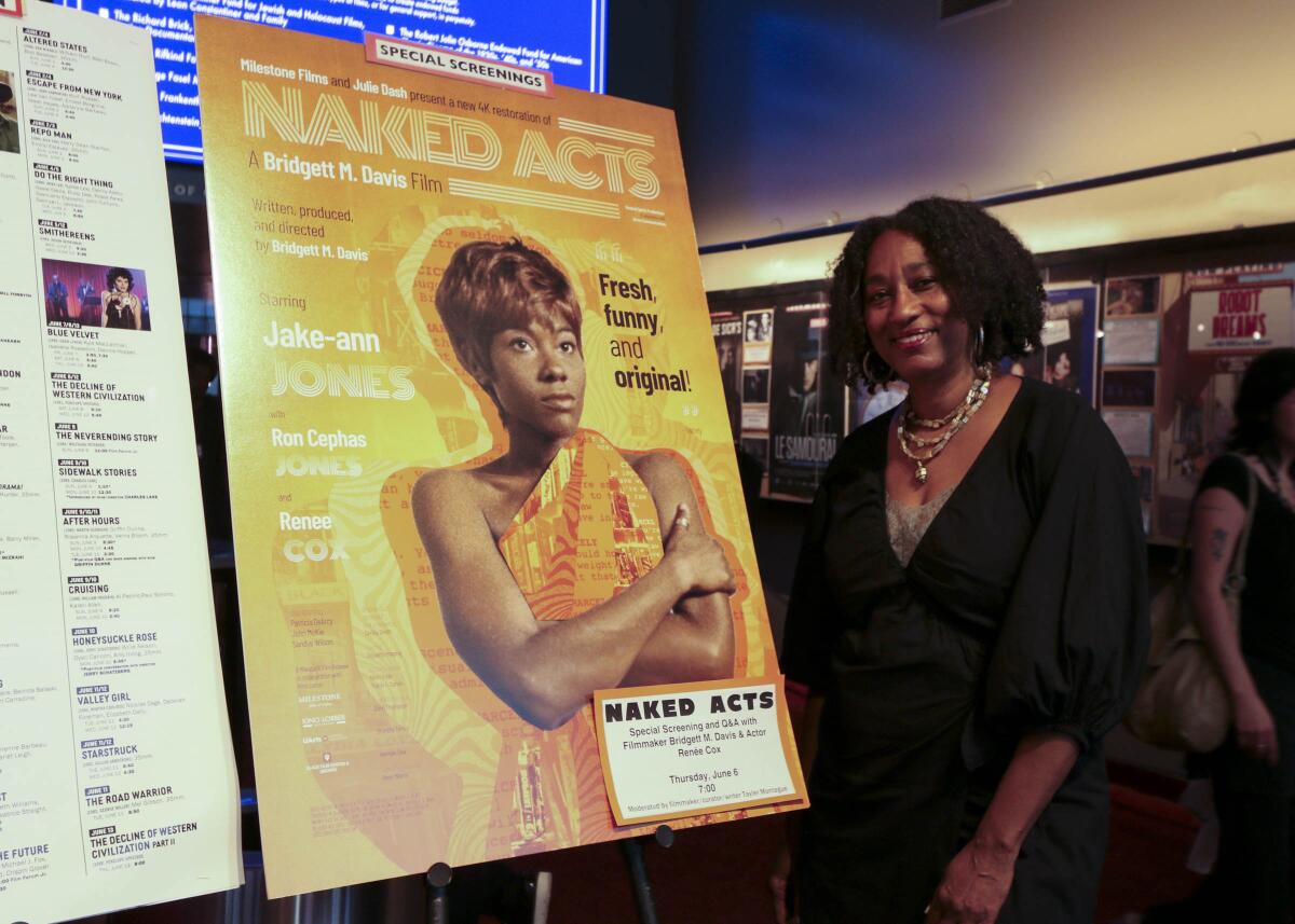 A smiling woman stands next to a movie poster.