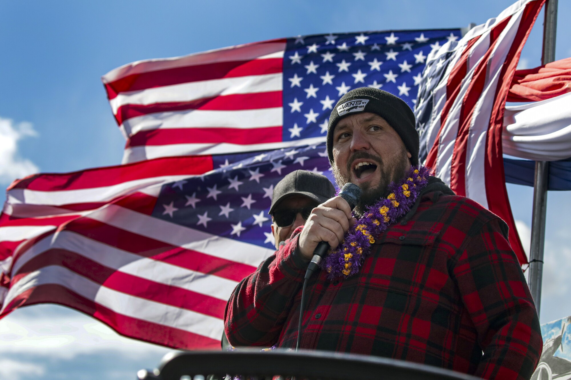 Il camionista Brian Brase parla a una manifestazione, con le bandiere americane dietro di lui