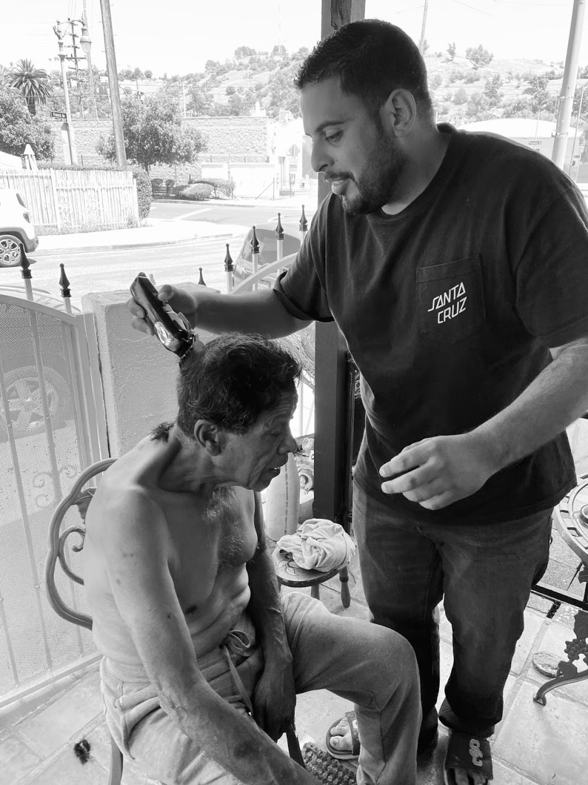 A man uses clippers to cut his father's hair on a porch