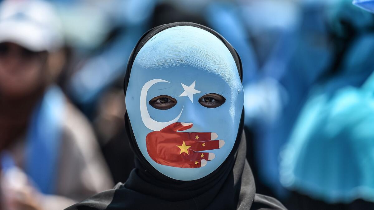 A demonstrator wears a mask painted with the colors of the East Turkestan flag and a hand bearing the colors of the Chinese flag at a July protest at the Chinese consulate in Istanbul.