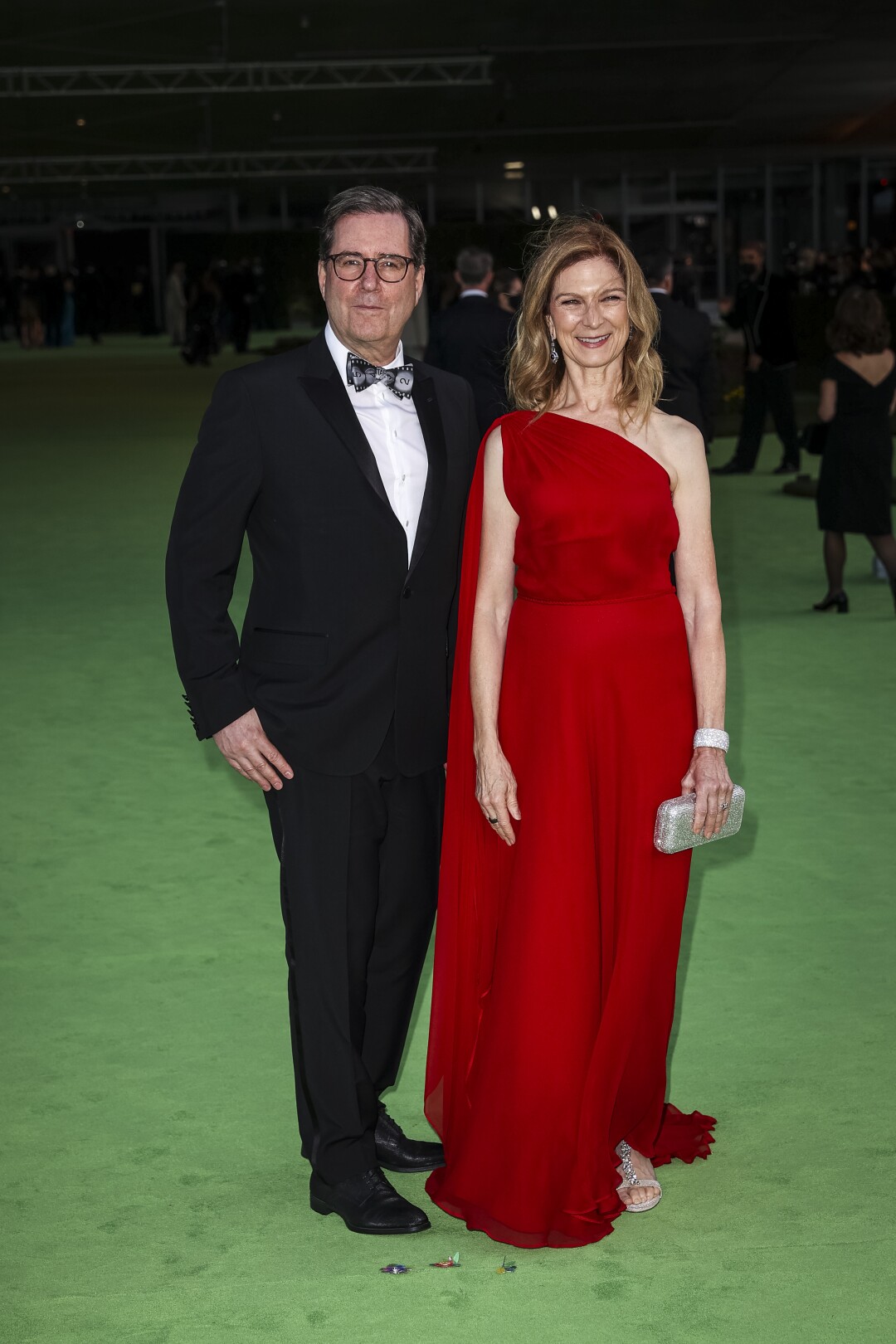 A man in a black suit and a woman in a red dress posing on a green carpet
