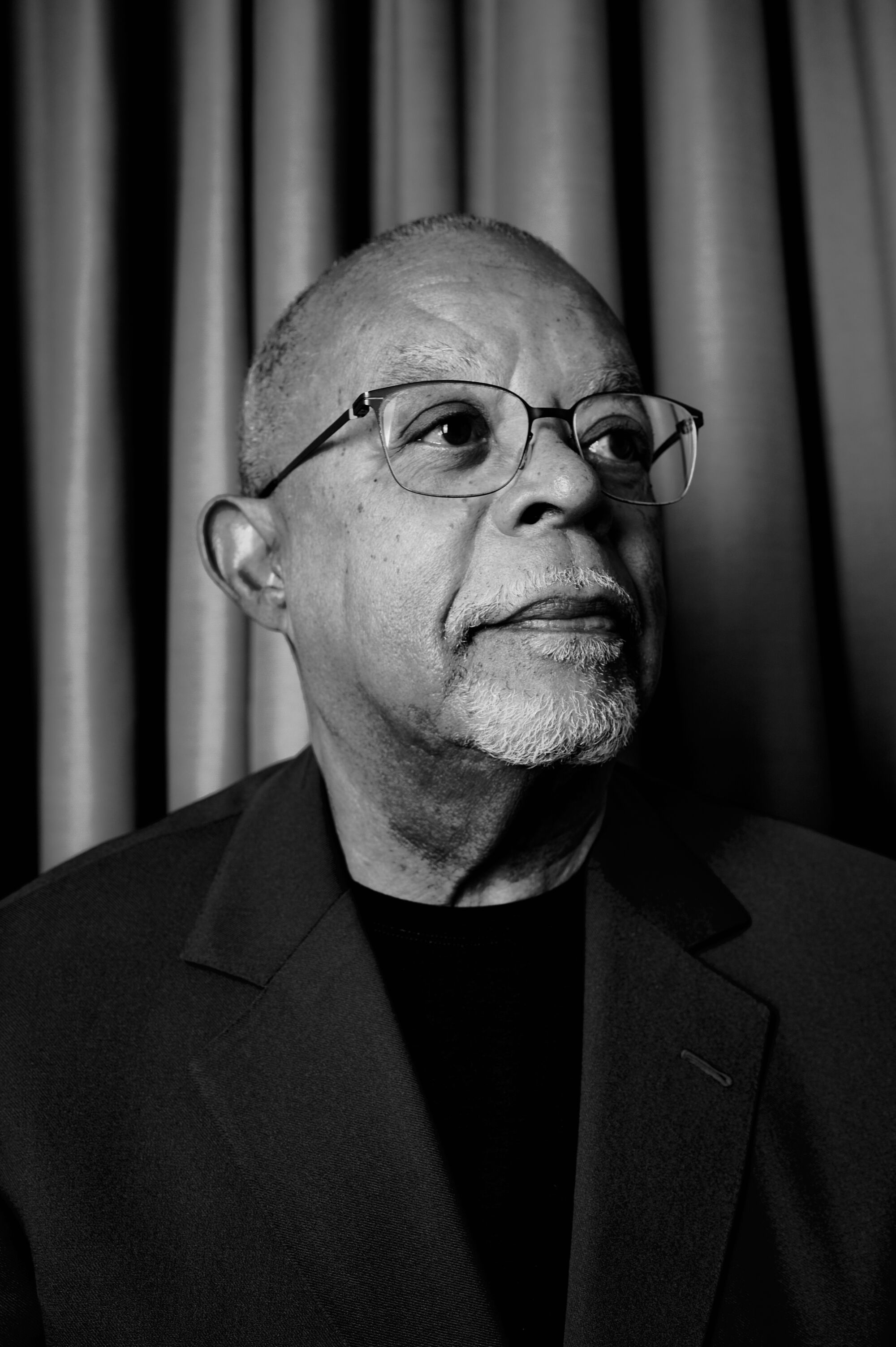 A black and white photo portrait of a man with a shaved head, glasses and a goatee.