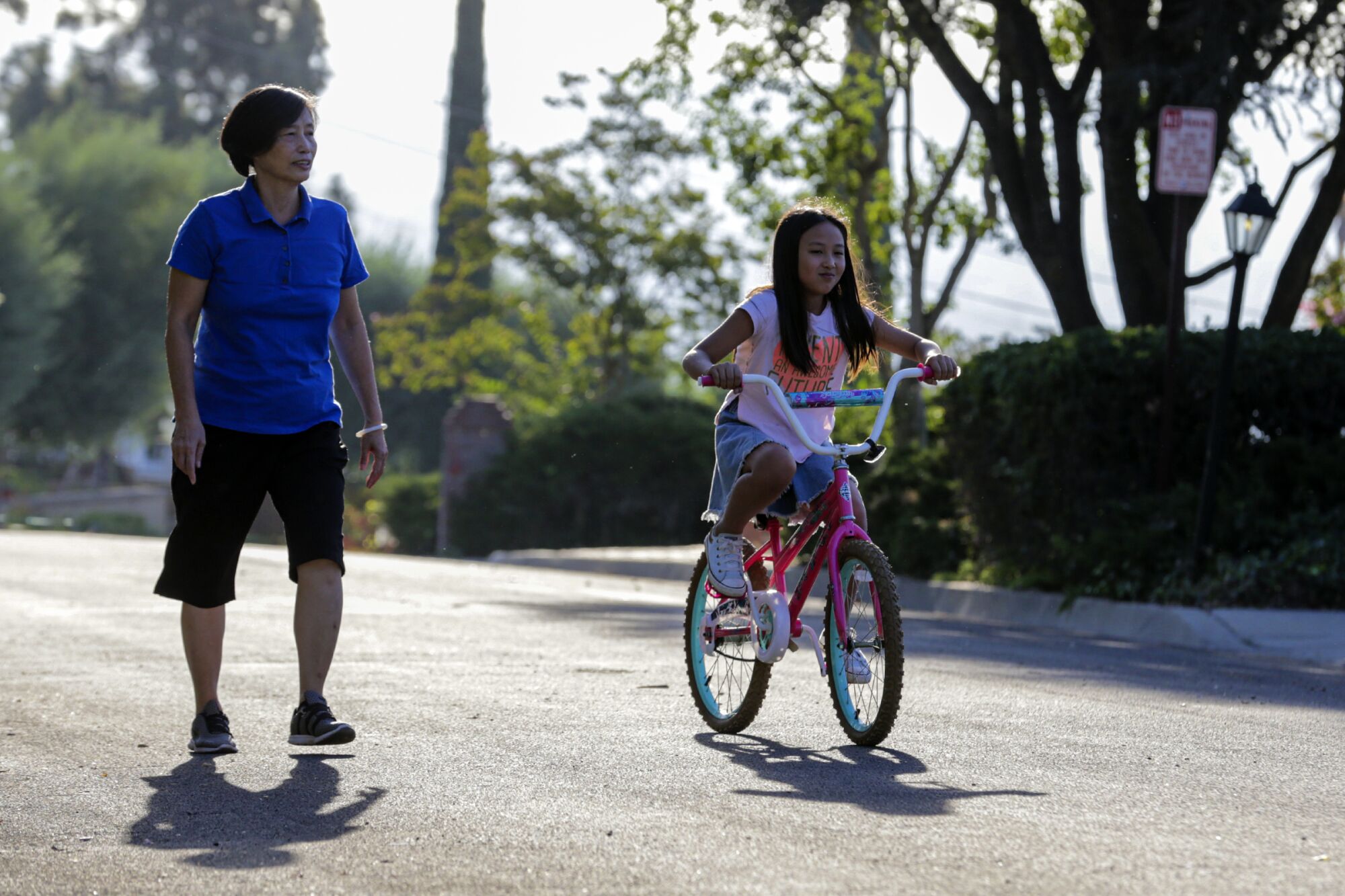 Yuyuan Lin walks with her 9-year-old granddaughter, Hannah, who rides a bicycle.