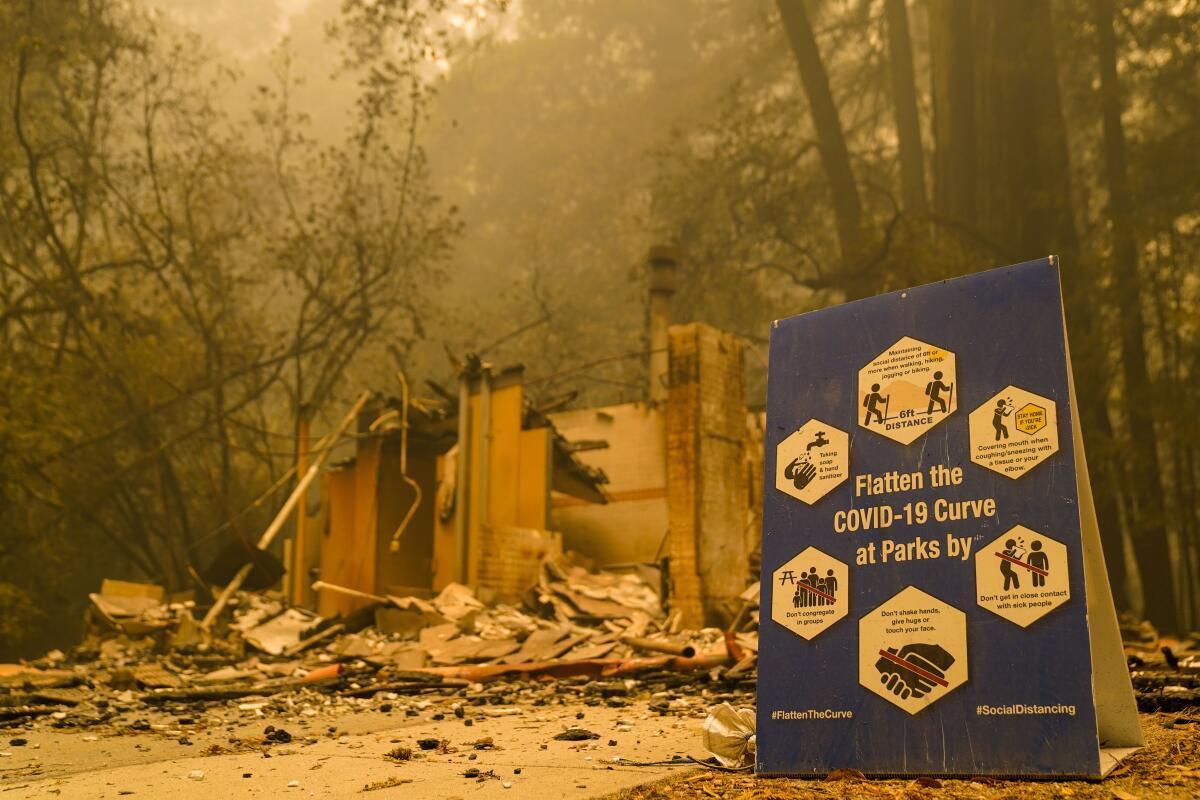 A COVID-19 sign sits in front of a burned structure at Big Basin Redwoods State Park in Boulder Creek, Calif.