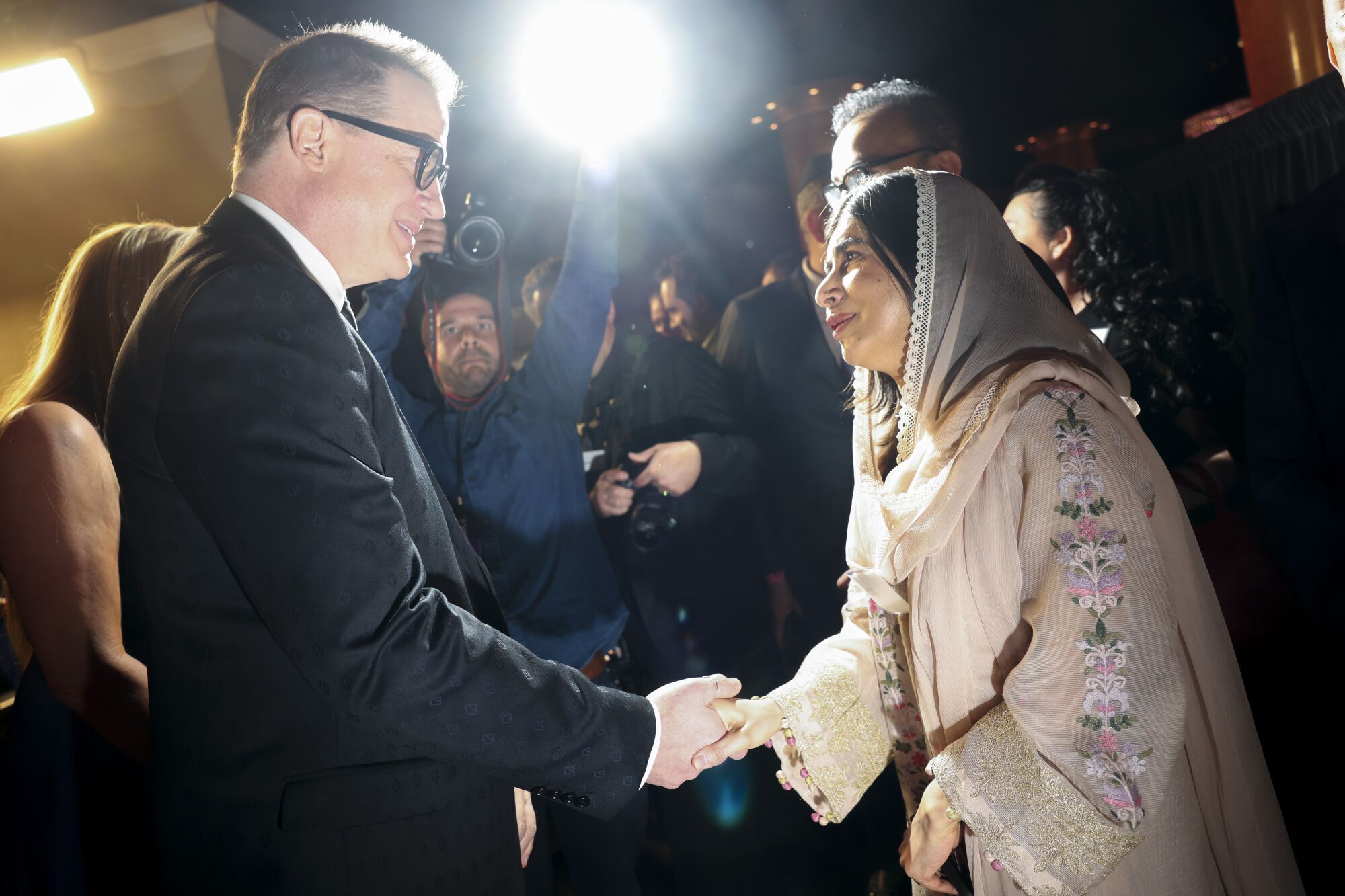 A man in a suit shakes hands with a woman in traditional Pakistani dress.