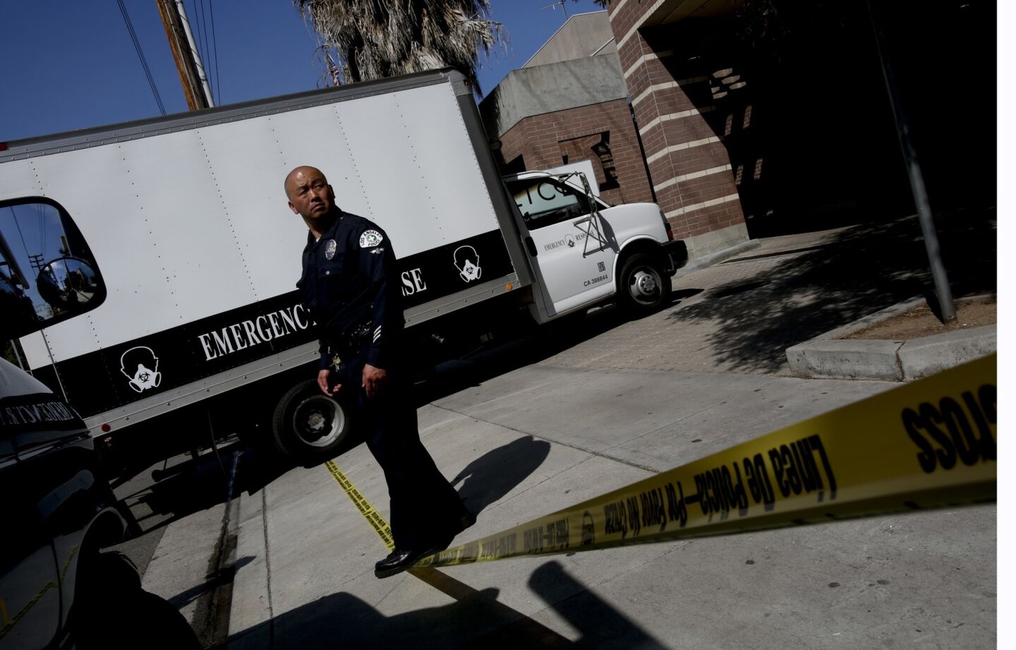 Los Angeles Police Officer Len Lai stands on yellow tape as an emergency response truck leaves an LAPD station in Mid-City L.A. where an officer was shot Monday night.