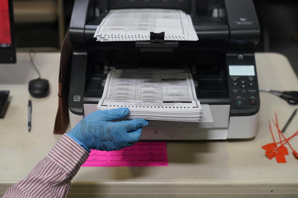 ARCHIVO - Un trabajador del condado carga boletas por correo en un escáner que registra los votos 
