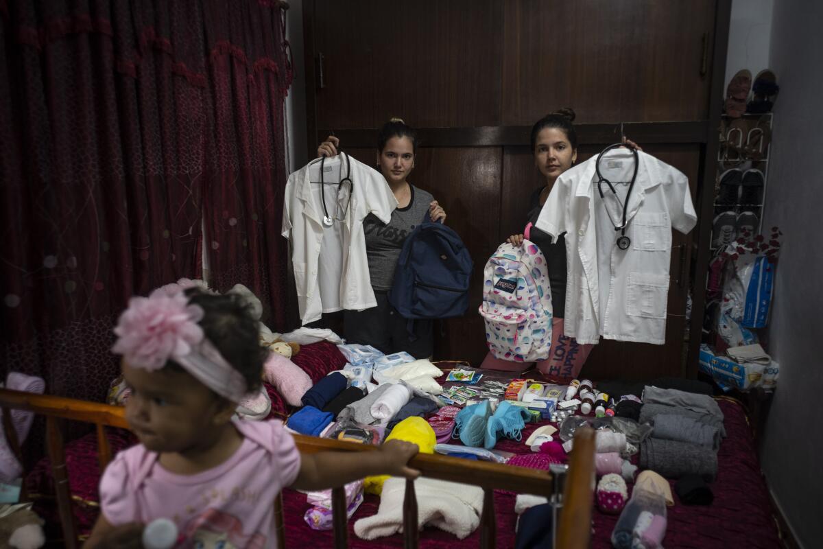 Women and a small girl occupy a bedroom filled with clothing and supplies. 