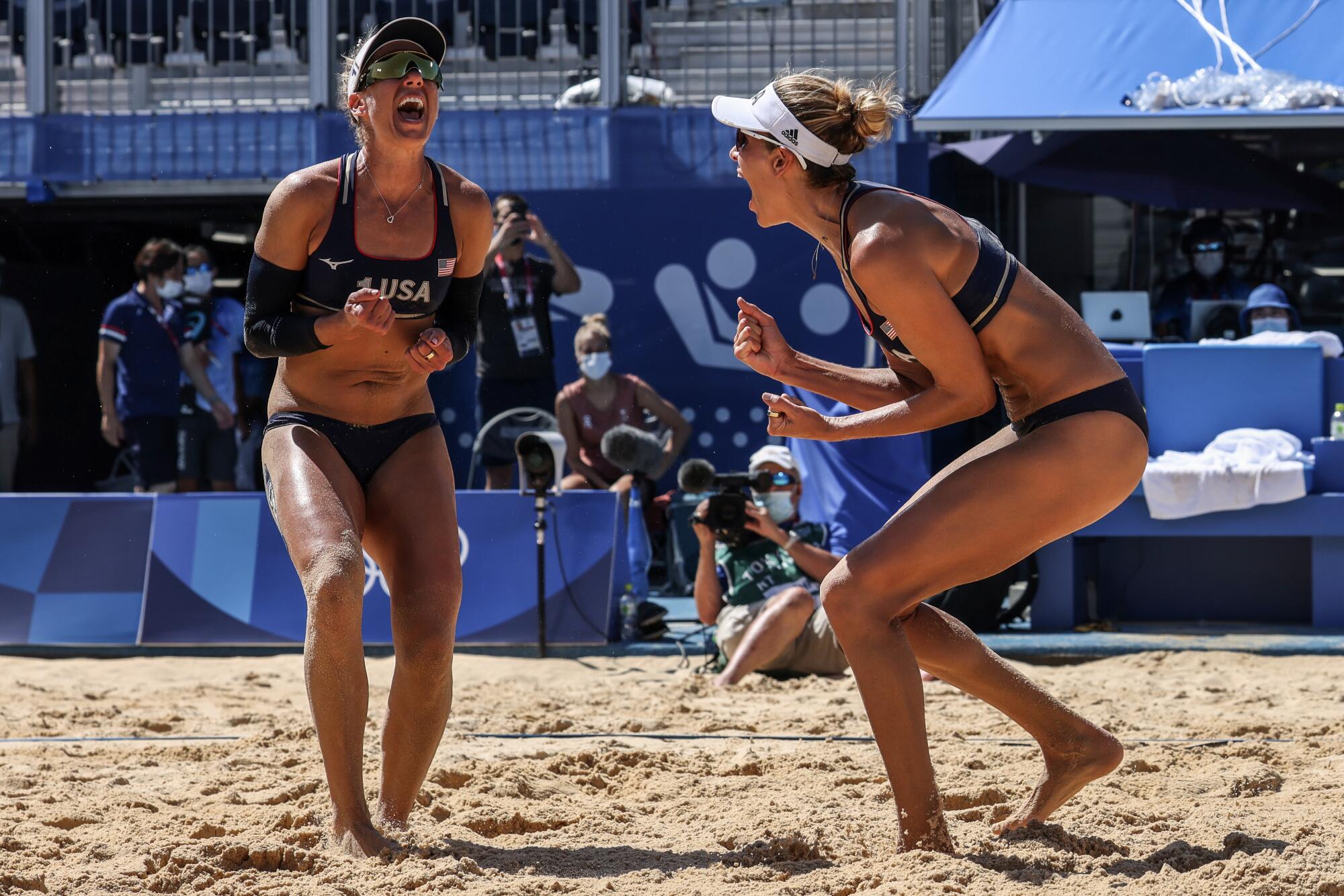 Women beach volleyball players shout in celebration on court.