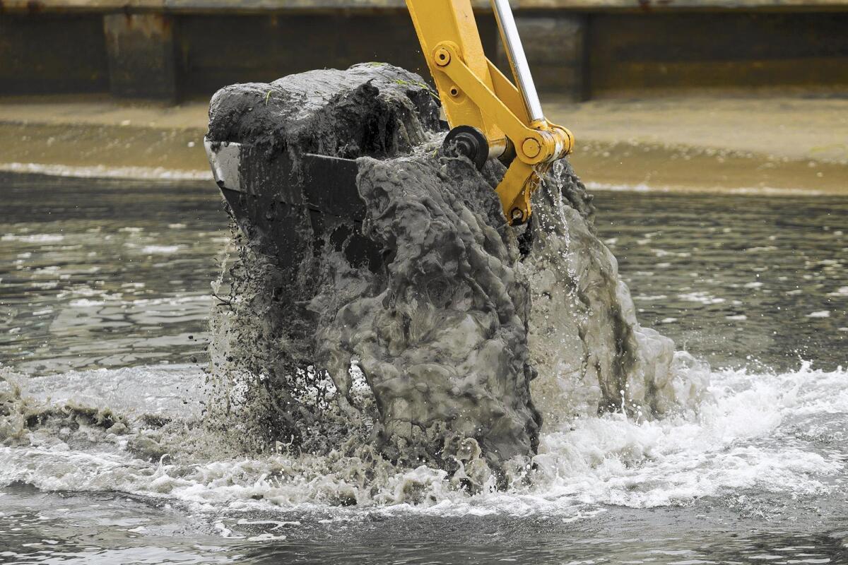 An excavator’s bucket filled with soil is removed from the Grand Canal between Balboa Island and Little Balboa Island on Thursday.