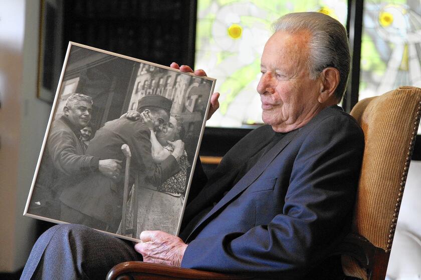 At his Beverly Hills home, movie producer Mace Neufeld holds his 1944 photograph of a wounded Pvt. Sam Macchia being welcomed home by his parents in New York City. The picture was taken by Neufeld when he was 16 and was on the short list for the 1945 Pulitzer Prize.