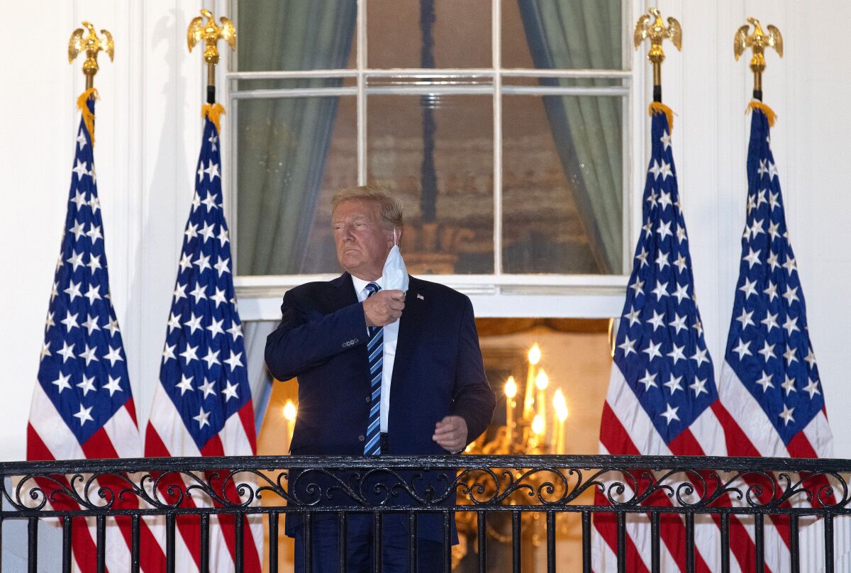 Trump, on a White House balcony, removes his mask.