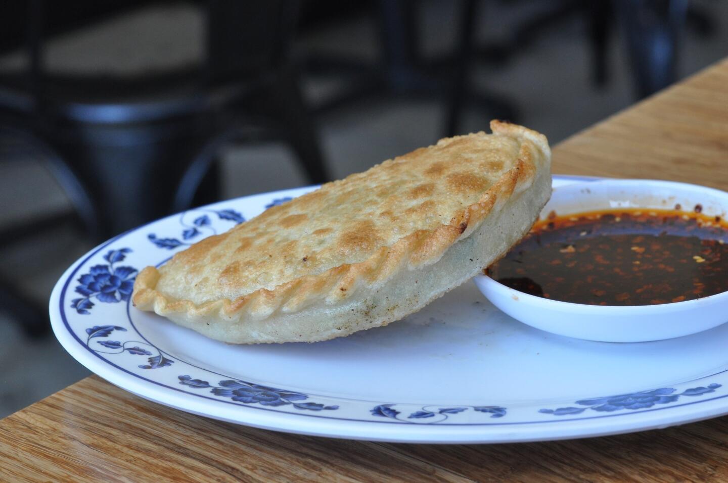 A meat pie at House of Bao, with the small bowl that came filled with spicy peanuts and is now filled with chiles and black vinegar.