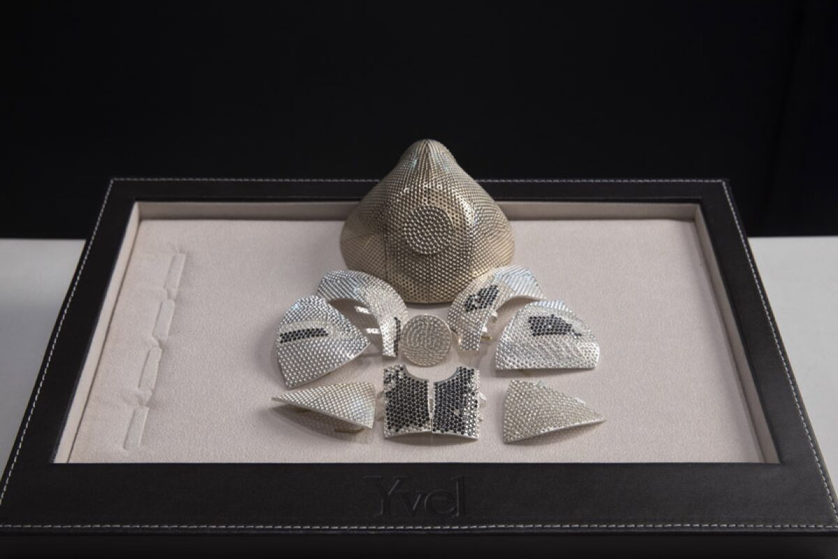 Several pieces of an 18-karat white gold mask are displayed in front of a model of the face covering.