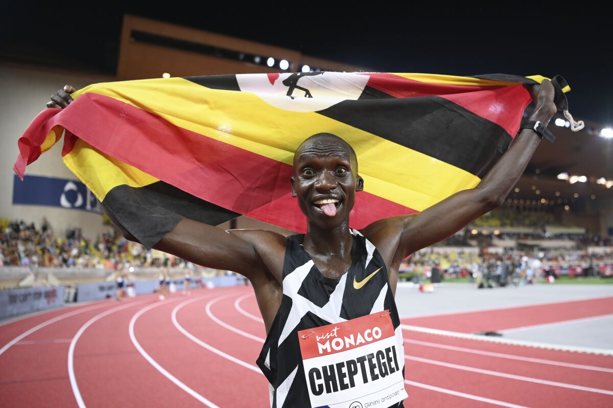 Joshua Cheptegei holds a Uganda flag and sticks his tongue out after winning the men's 5,000 meters at the Tokyo Olympics.