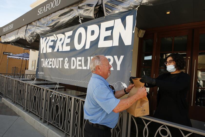 VENTURA, CA - APRIL 22: Greg Thomas picks up his lunch from Samantha Madec at Lure Fish House on South California Street in downtown Ventura Wednesday morning as Ventura County on Saturday modified its stay-at-home order to permit some businesses to reopen and some gatherings to take place for the first time since the restrictions were issued to fight the spread of the coronavirus COVID-19. Ventura on Wednesday, April 22, 2020 in Ventura, CA. (Al Seib / Los Angeles Times)