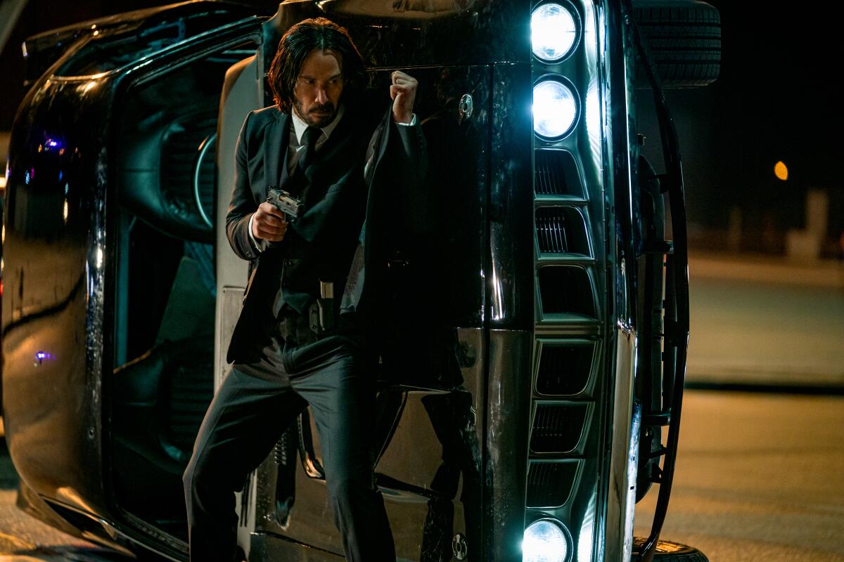 John Wick, wearing a suit and holding a gun