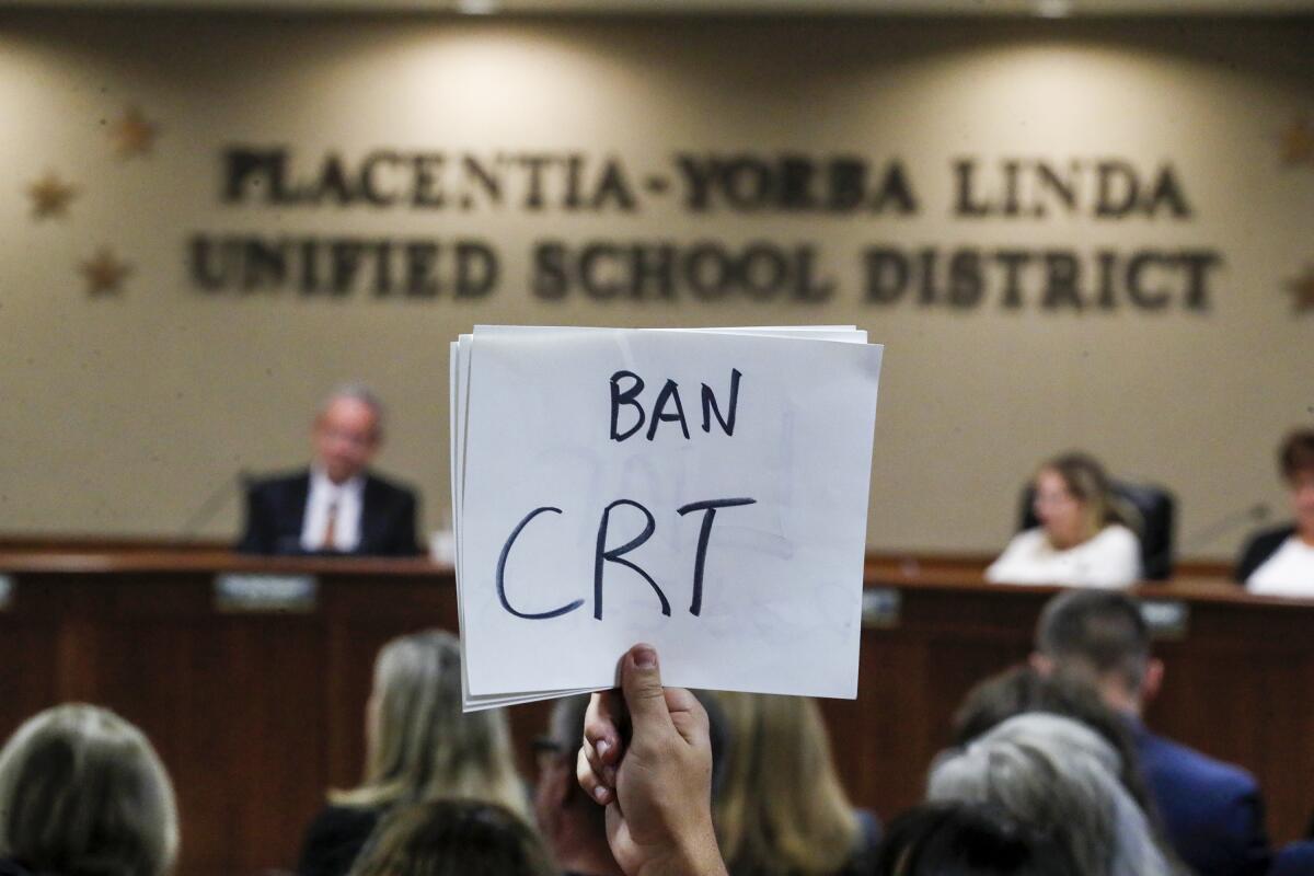 Someone holds up a sign opposing critical race theory at a board meeting