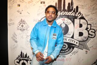 Justin Combs is posing in jeands, a sky blue leather jacket and brown sunglasses with his hands resting in front of him