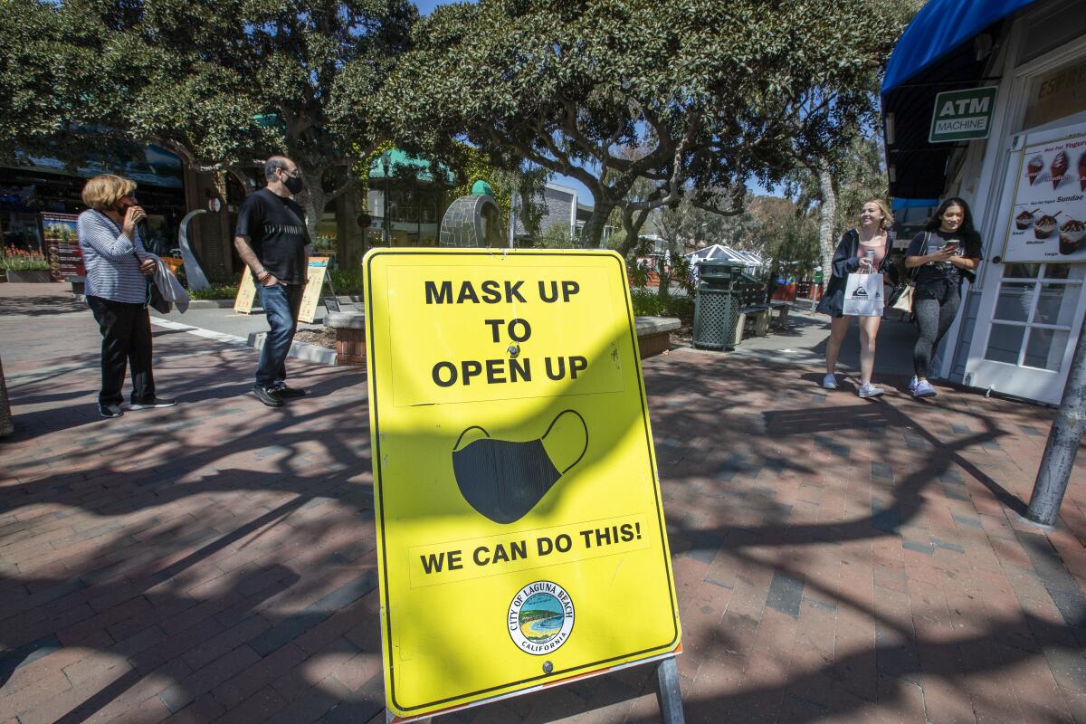 People on a walkway near a sign that reads, "Mask up to open up: We can do this!"