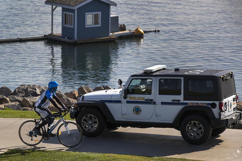 LONG BEACH, CA - December 09: A bicyclist wearing a face cover rides past Long Beach Police on patrol at ShoreLine Aquatic Park in Long Beach Wednesday, Dec. 9, 2020. Long Beach City Council is considering ramping up enforcement for people who are not wearing masks and how it has been handling the pandemic lately, since the city has its own public health department, apart from LA County. (Allen J. Schaben / Los Angeles Times)