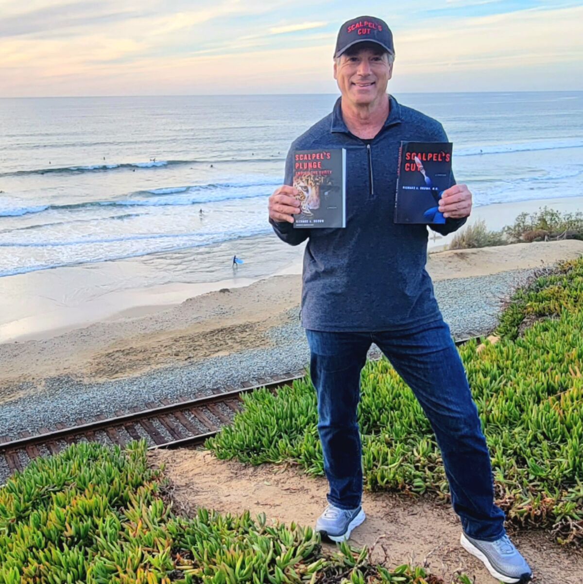 Author Dr. Richard Brown holding his novels above the beach in Del Mar.
