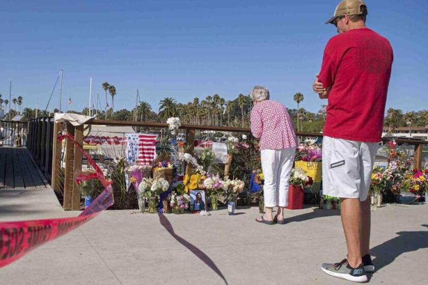 Dos personas observan un monumento conmemorativo improvisado colocado en honor de las víctimas de un incendio en un bote de buceo mientras las autoridades allanaban las oficinas de Truth Aquatics, la compañía propietaria de la embarcación, en Santa Barbara, California.