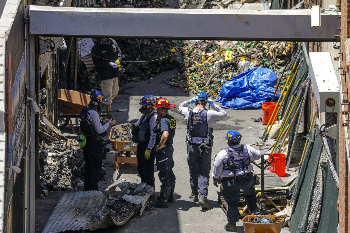 Men in fire helmets sift through piles of debris at a scorched building site.