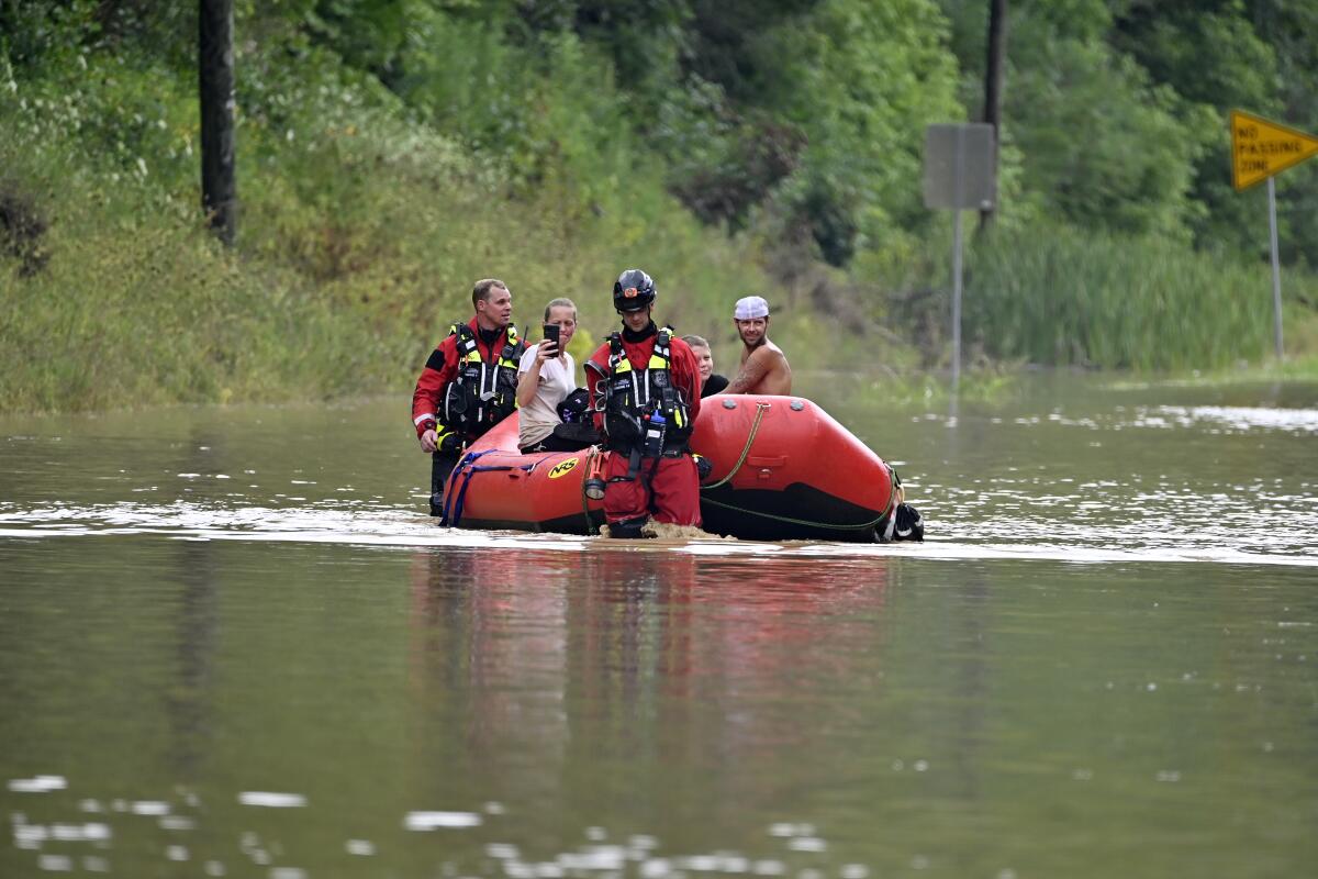 Rescuers in water up to their knees pull people in an inflatable boat across a flooded road.
