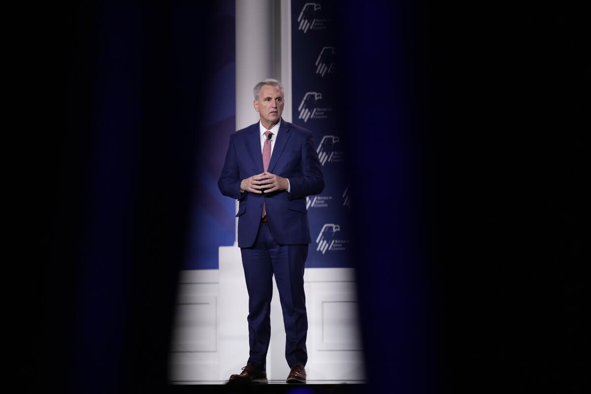 A man holding his hands together and standing in front of a backdrop on a stage.