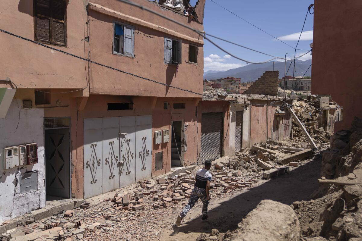 A man runs down a rubble-strewn street lined with buildings in terra-cotta colors