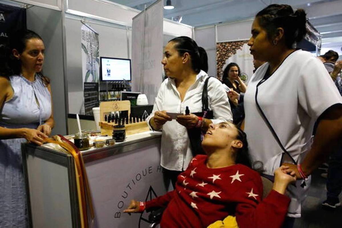 Claudia Gracia (c) escucha a una vendedora junto a su hija, que sufre parálisis cerebral y está en silla de ruedas, durante la 4ta edición de la feria de cannabis ExpoWeed en Ciudad de México.