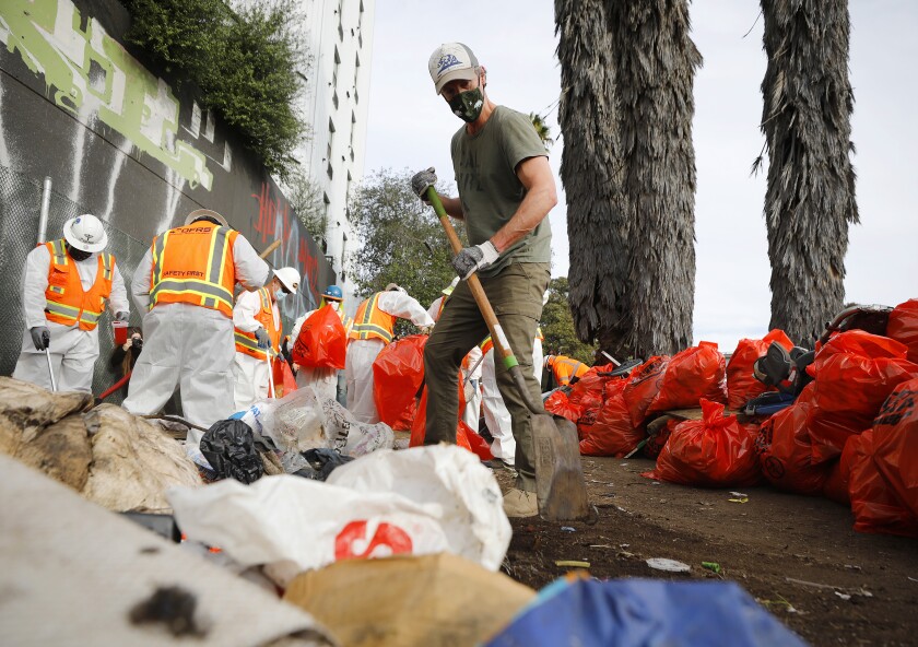 Gov. Gavin Newsom helps clean up a homeless encampment alongside Interstate 5 and G Street in San Diego on Wednesday.