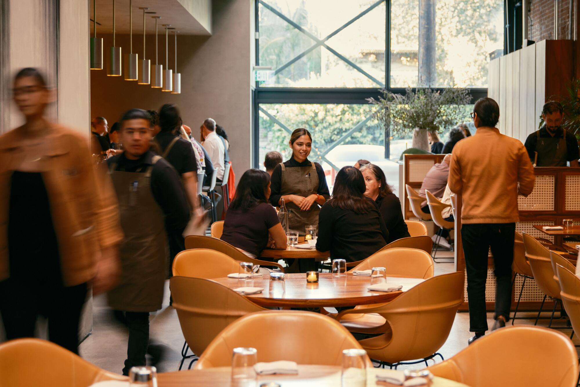 People walk past tables ringed with bucket chairs.