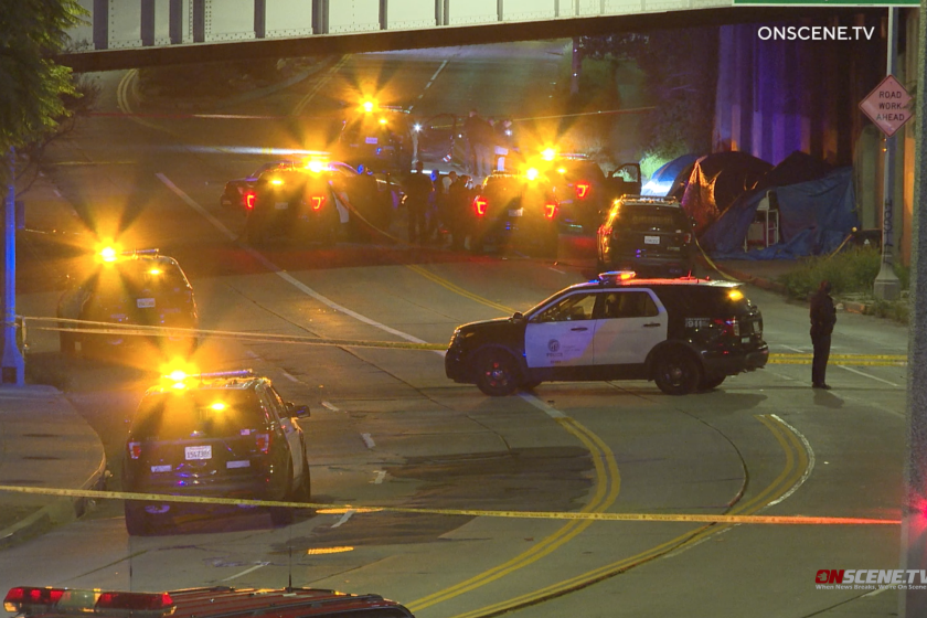 Six police cruisers are seen beneath a city overpass with lights flashing. 