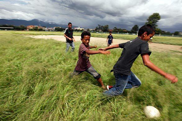 Boys play with a soccer ball as monsoon clouds hover over Katmandu, Nepal.