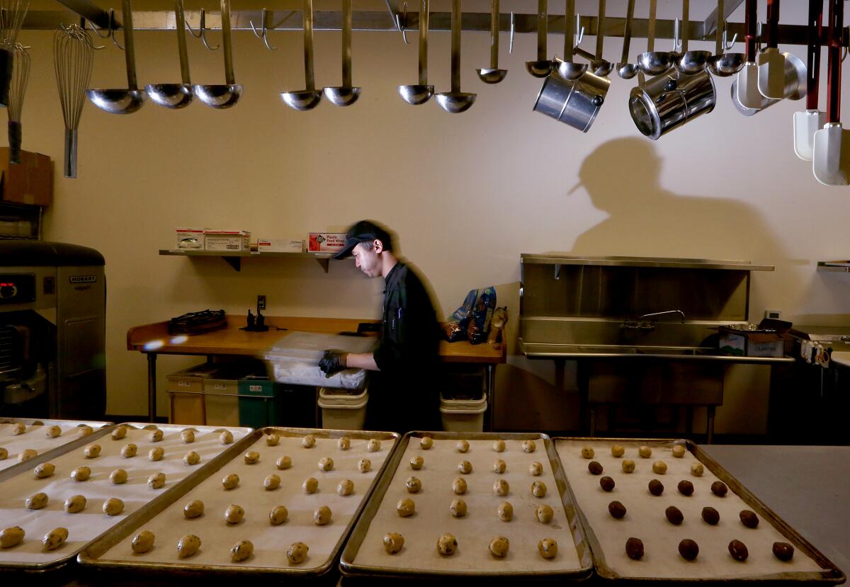 A man stands near trays of food to be cooked.