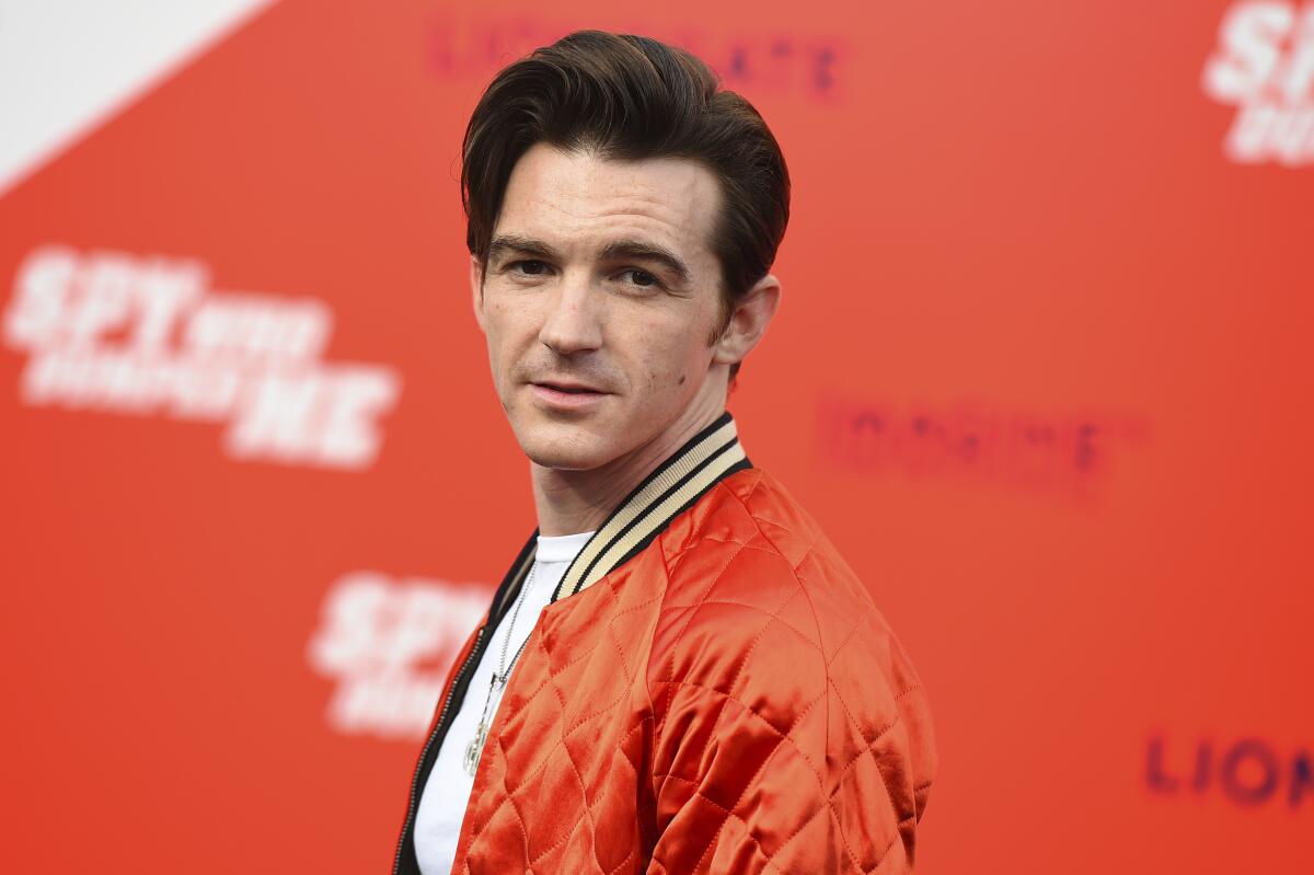 Drake Bell wearing an orange bomber jacket poses at a movie premiere