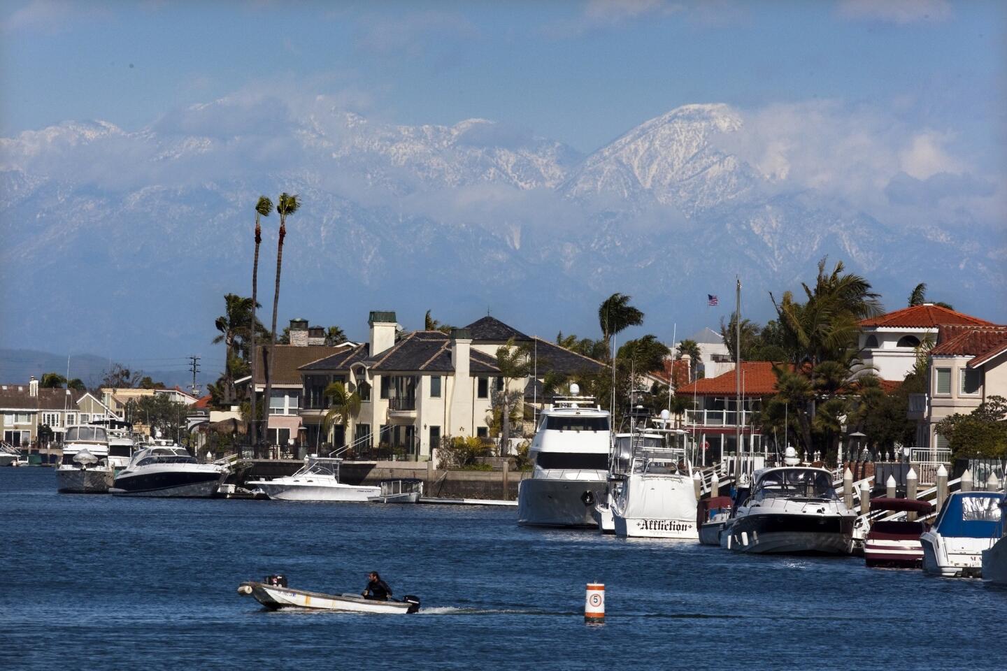 A motor boat cruises Huntington Harbour in Huntington Beach against a backdrop of the recently snowcapped San Gabriel Mountains.