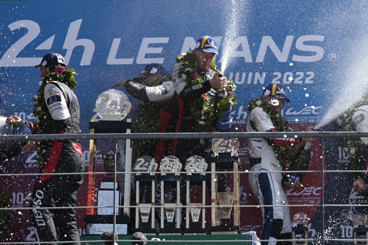 Sebastien Buemi of Switzerland, left, Brendon Hartley of New Zealand, center, and Ryo Hirakawa of Japan, center left behind, spray Champagne after winning the 24-hHour Le Mans endurance race in their Toyota Gazoo Racing GRO10 Hybrid in Le Mans, western France, Sunday June 12, 2022. (AP Photo/Jeremias Gonzalez)