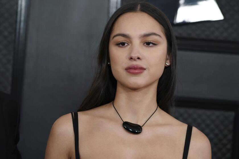 Olivia Rodrigo posing in a black, chunky necklace against a black background