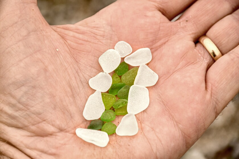 Green and white pieces of sea glass in the palm of a hand