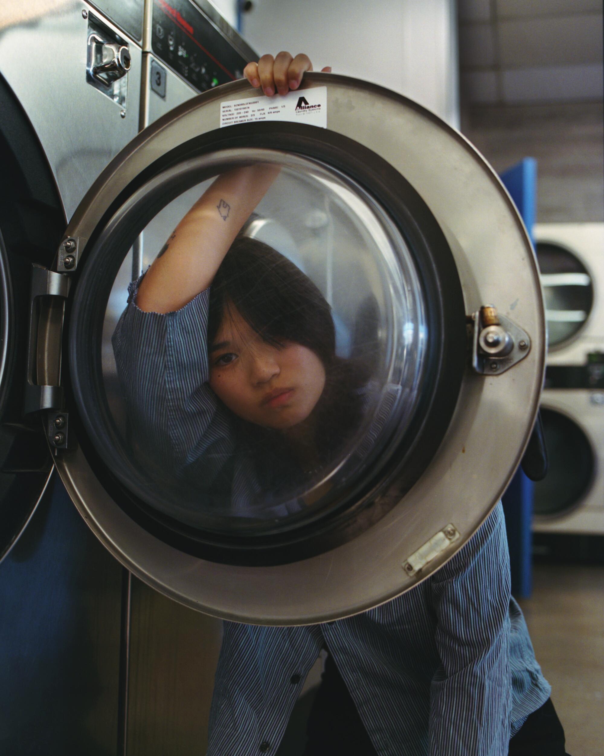 A woman is photographed looking through an open dryer door.