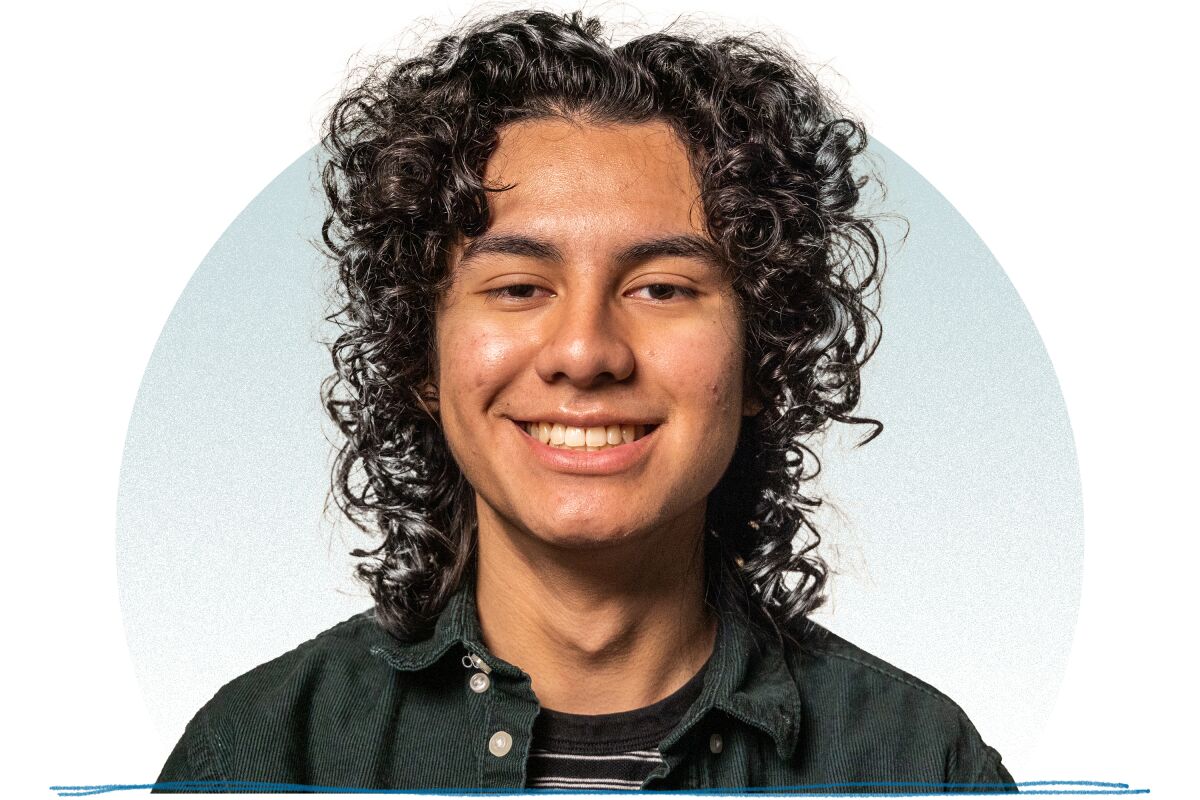 A young man with curly dark hair and a dark button down shirt smiling for a portrait.
