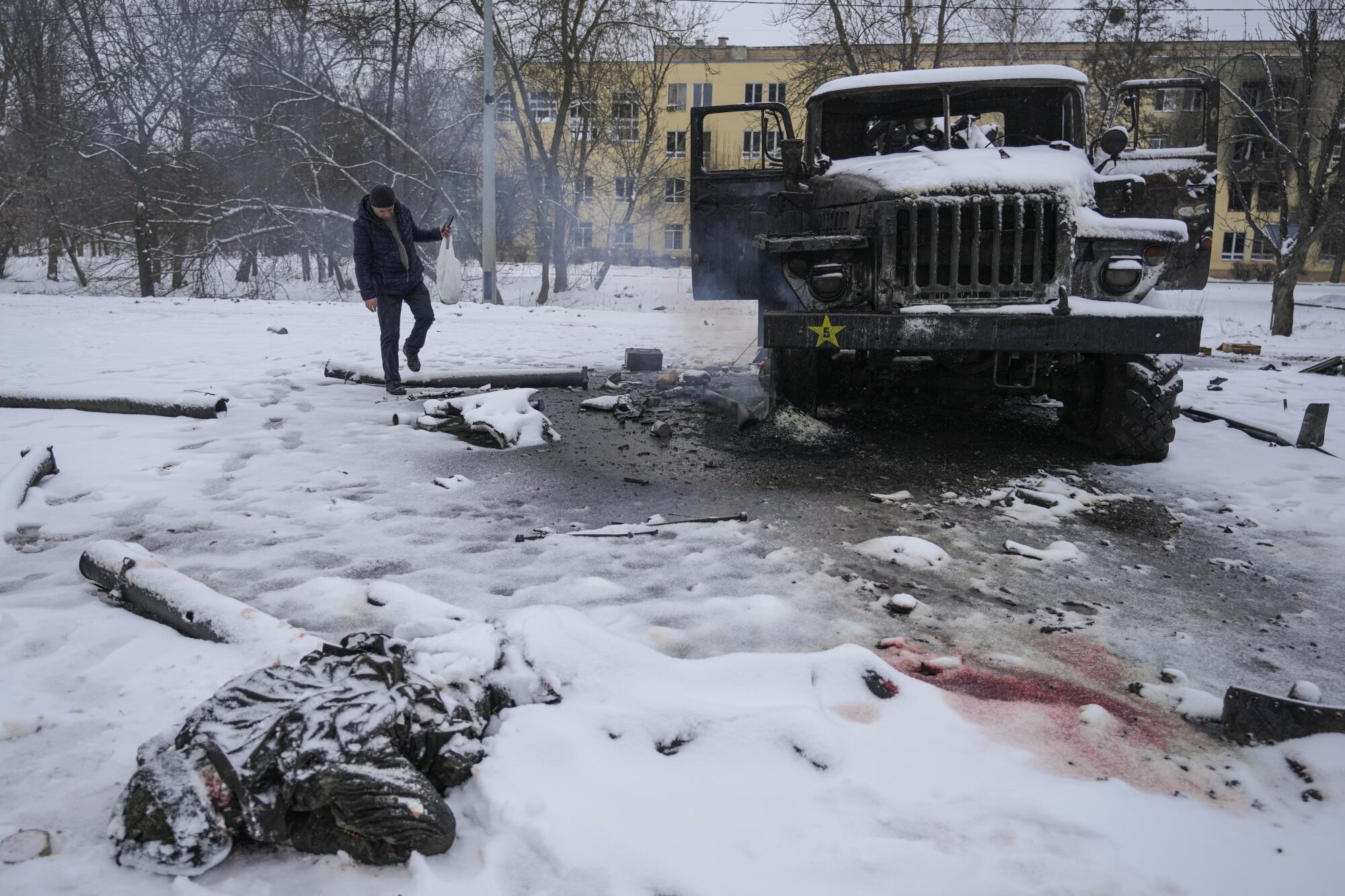 The body of a soldier in the snow near a military vehicle.