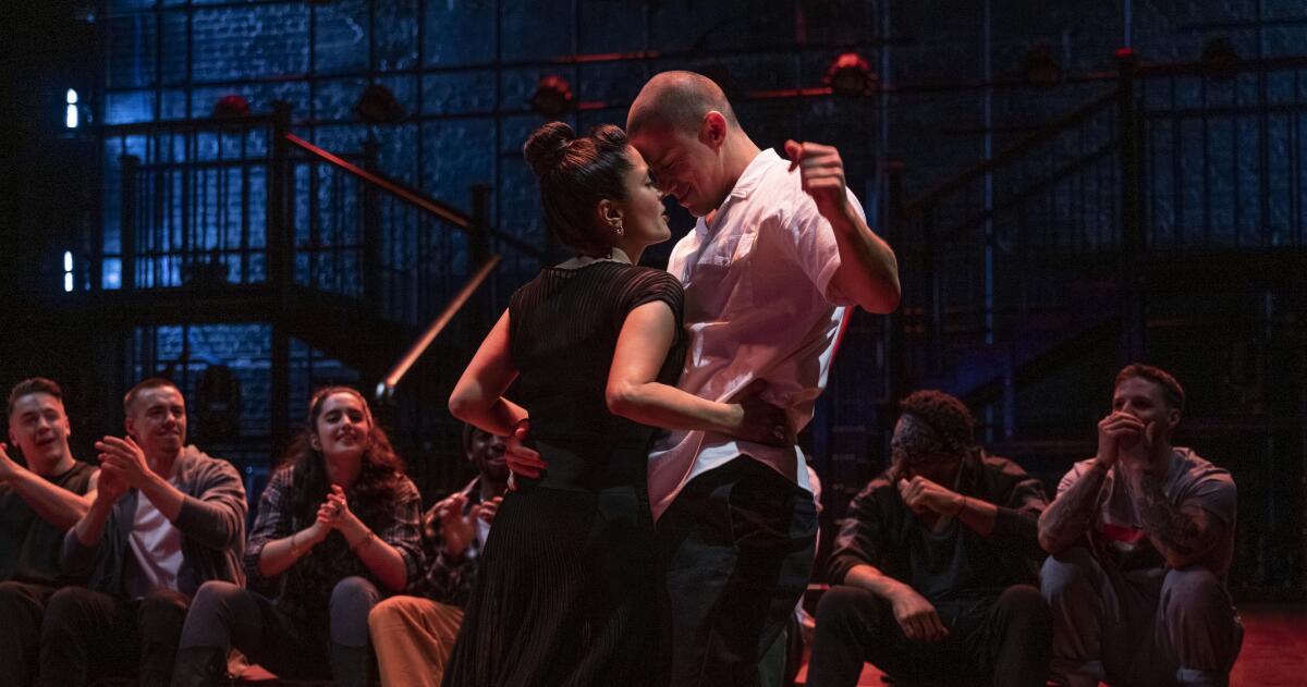 A woman and a man dance close together while people watch and clap 
