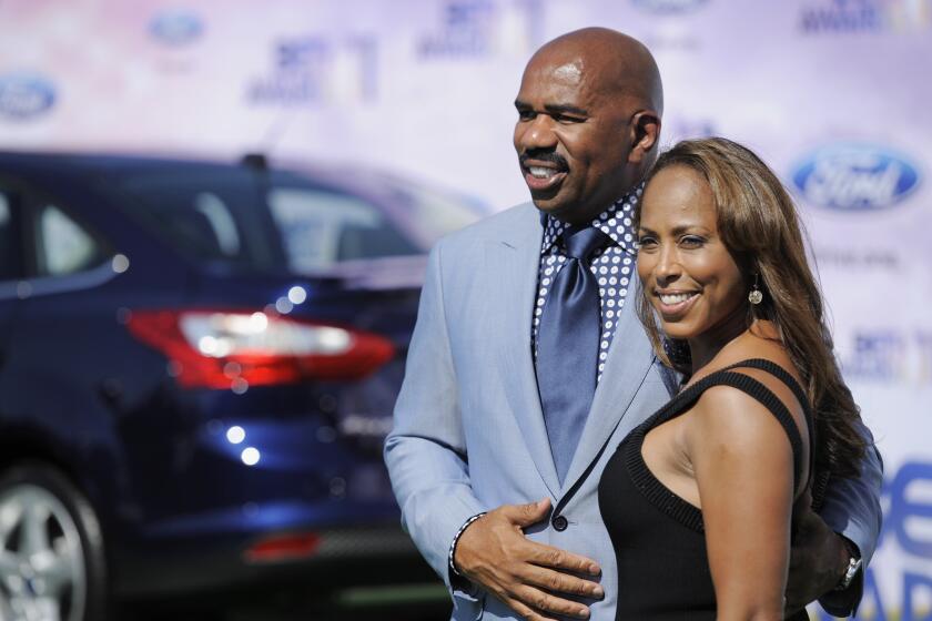 Steve Harvey and Marjorie Harvey smiling and posing together in formal attire in front of a car